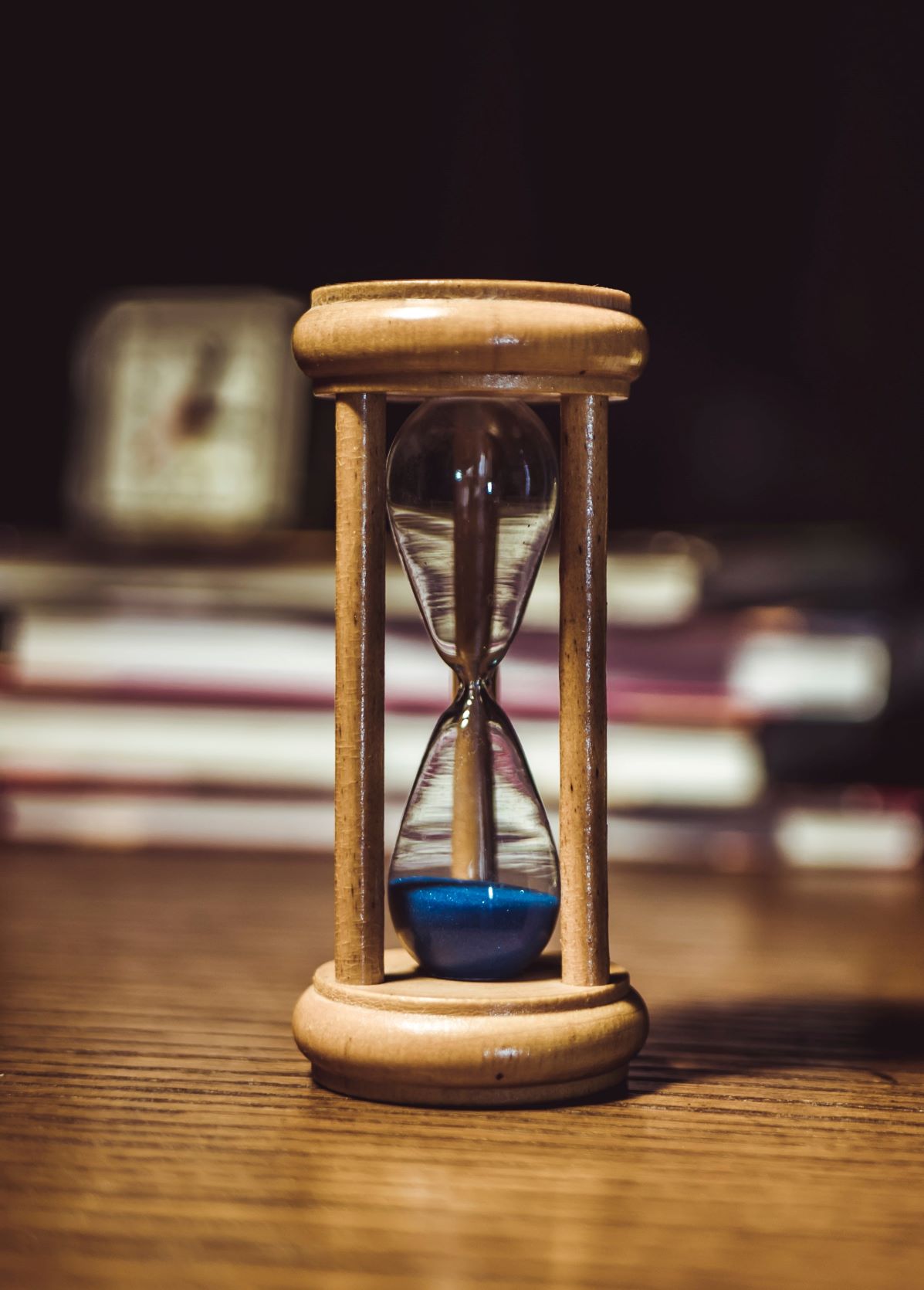 An hourglass with books and a clock in the background
