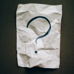 A crumpled piece of paper on a dark background. There is a large question mark on the paper.