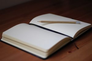 A picture of a notebook lying open on a blank page, with a pencil resting on the page