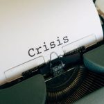 A typewriter with the word 'crisis' in the centre of a white sheet of paper