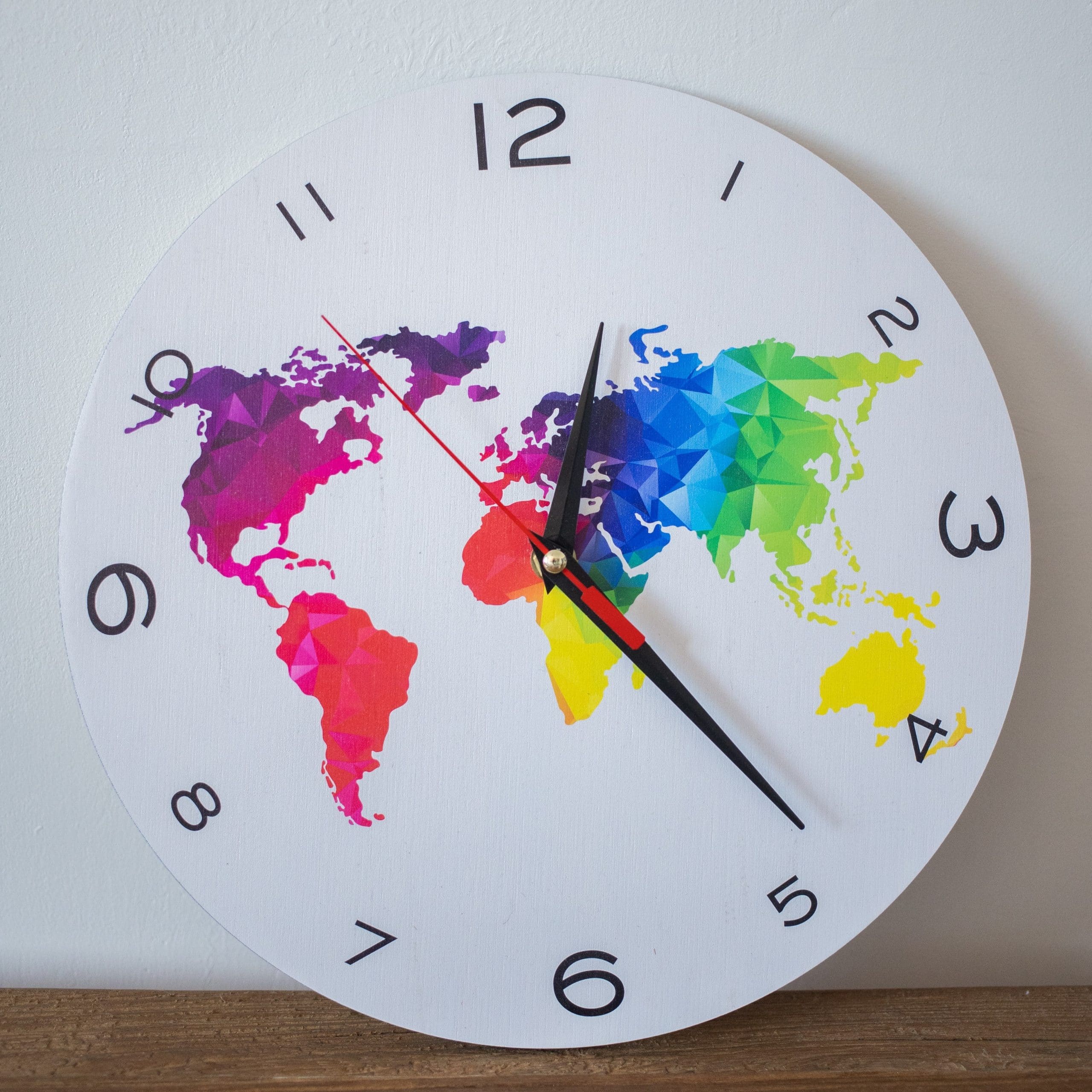 A white analogue clock with a stylised map of the world in rainbow colours