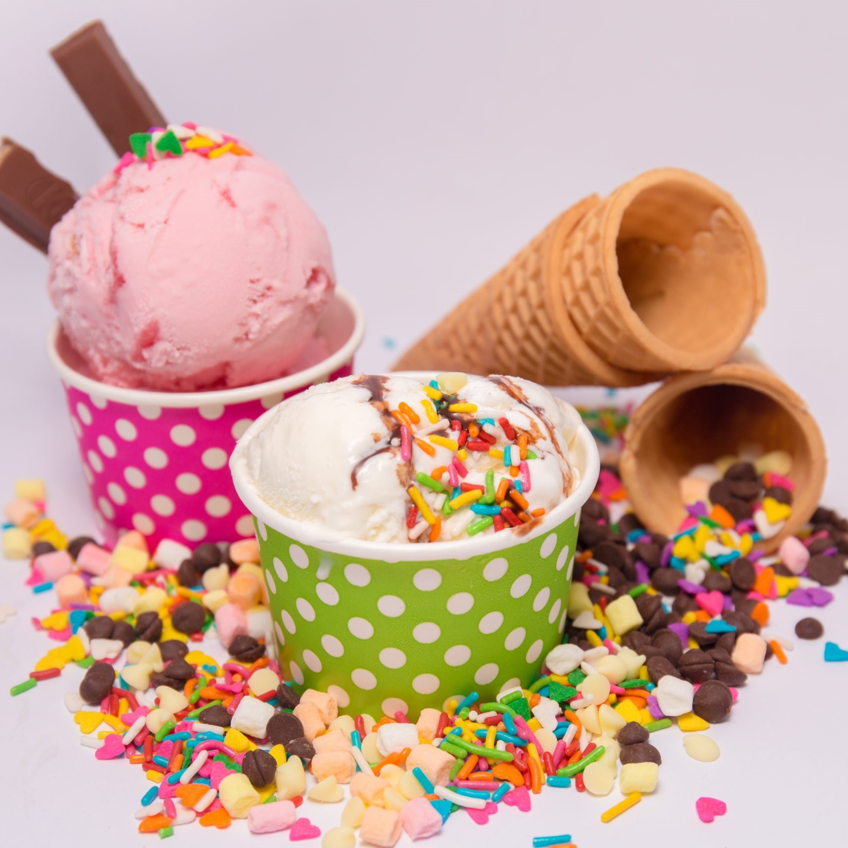 Two icecream cups, with cones and toppings scattered around