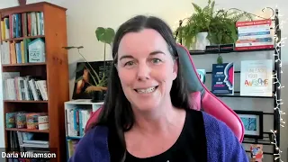 Still image from a webinar, showing a dark-haired woman wearing a black top and purple cardigan sitting in front of several bookshelves. She is smiling and about to say something.
