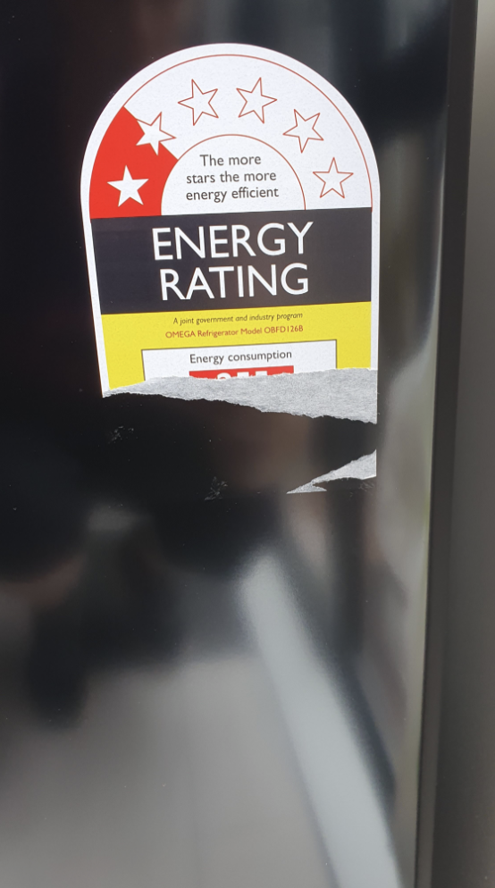 A partially-torn energy label on a fridge. Cheap decisions.