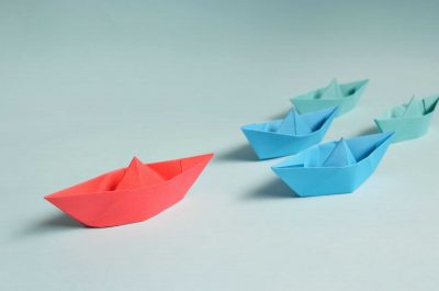 Different coloured paper boats on a white background