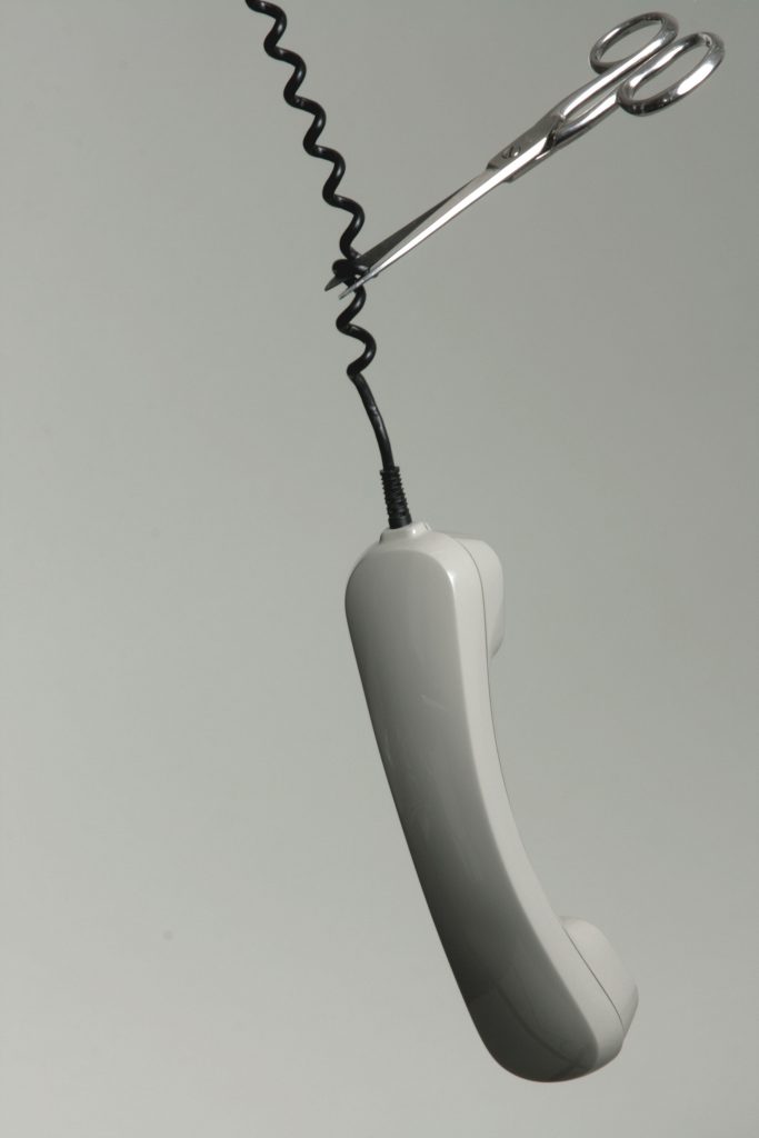 A corded telephone swinging upside-down with scissors cutting the cable