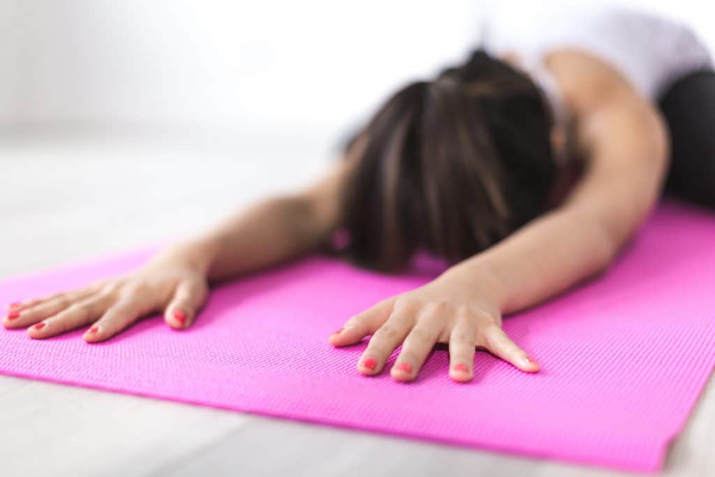 A woman kneeling on a pink yoga mat, stretching forward with her face near the ground