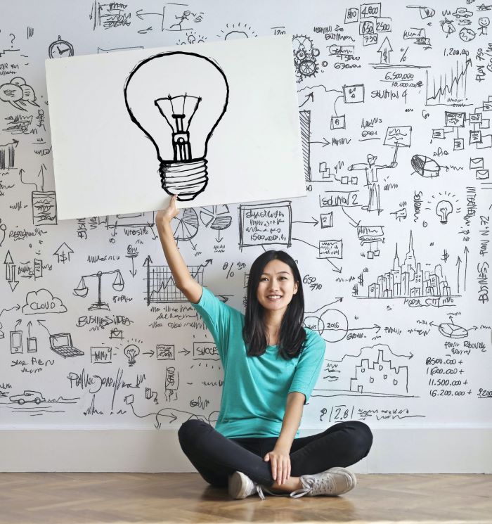 Woman sitting in front of a wall holding a drawing of a light bulb