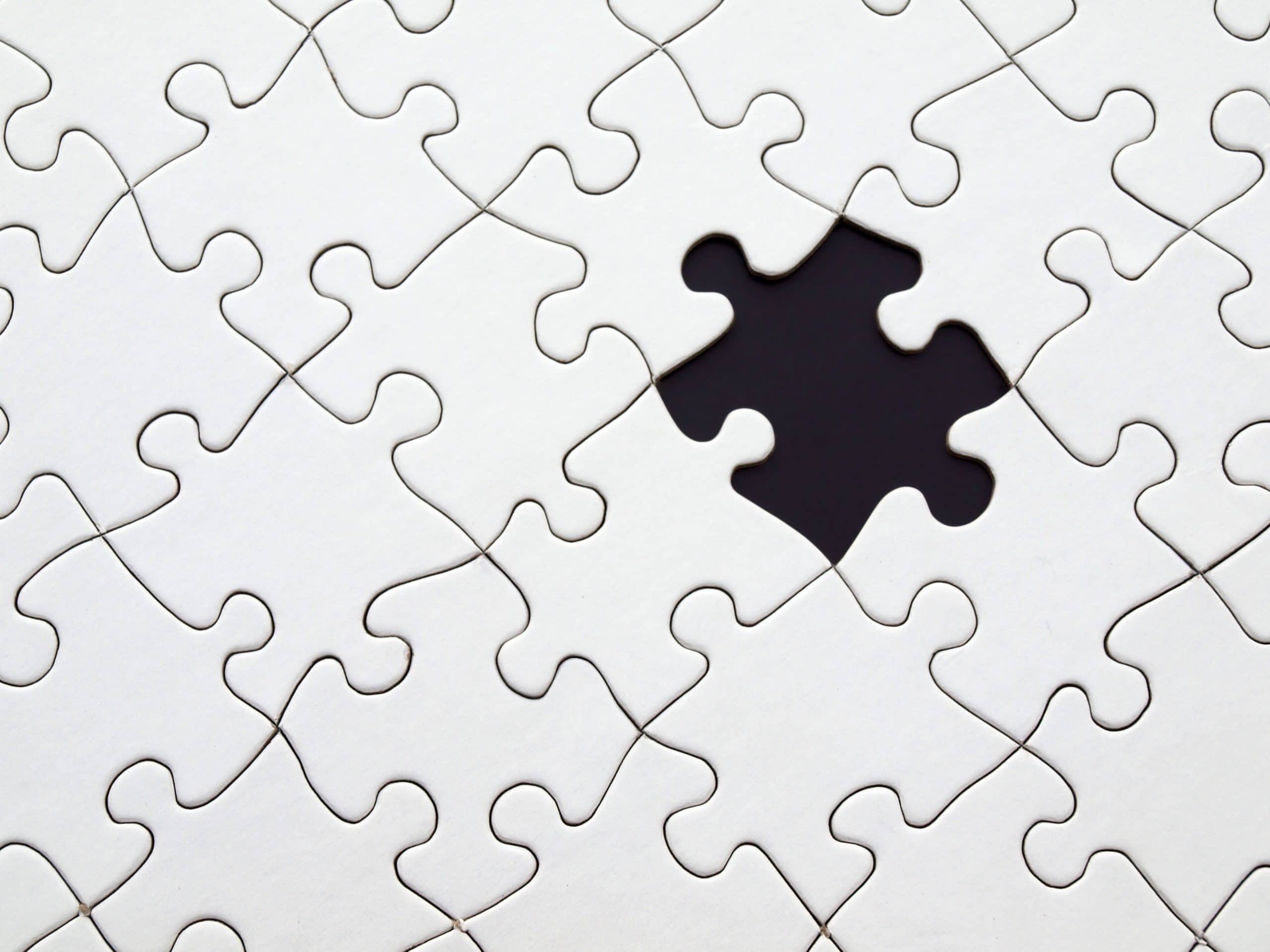 A photo of a white jigsaw puzzle on a black background, with a piece missing