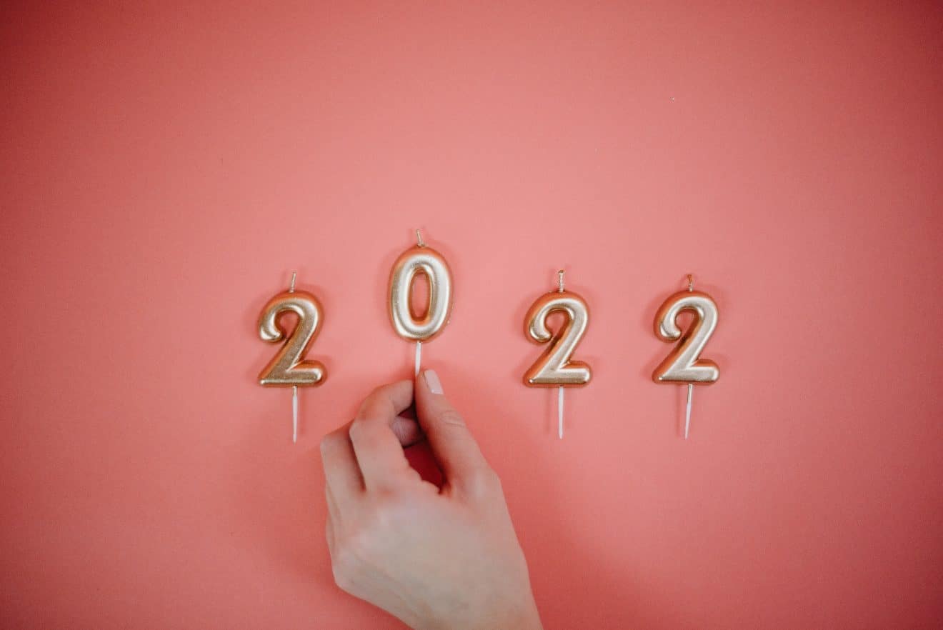 A hand positionining the "0" candle, which spells out 2022 in golden candles on a peach background