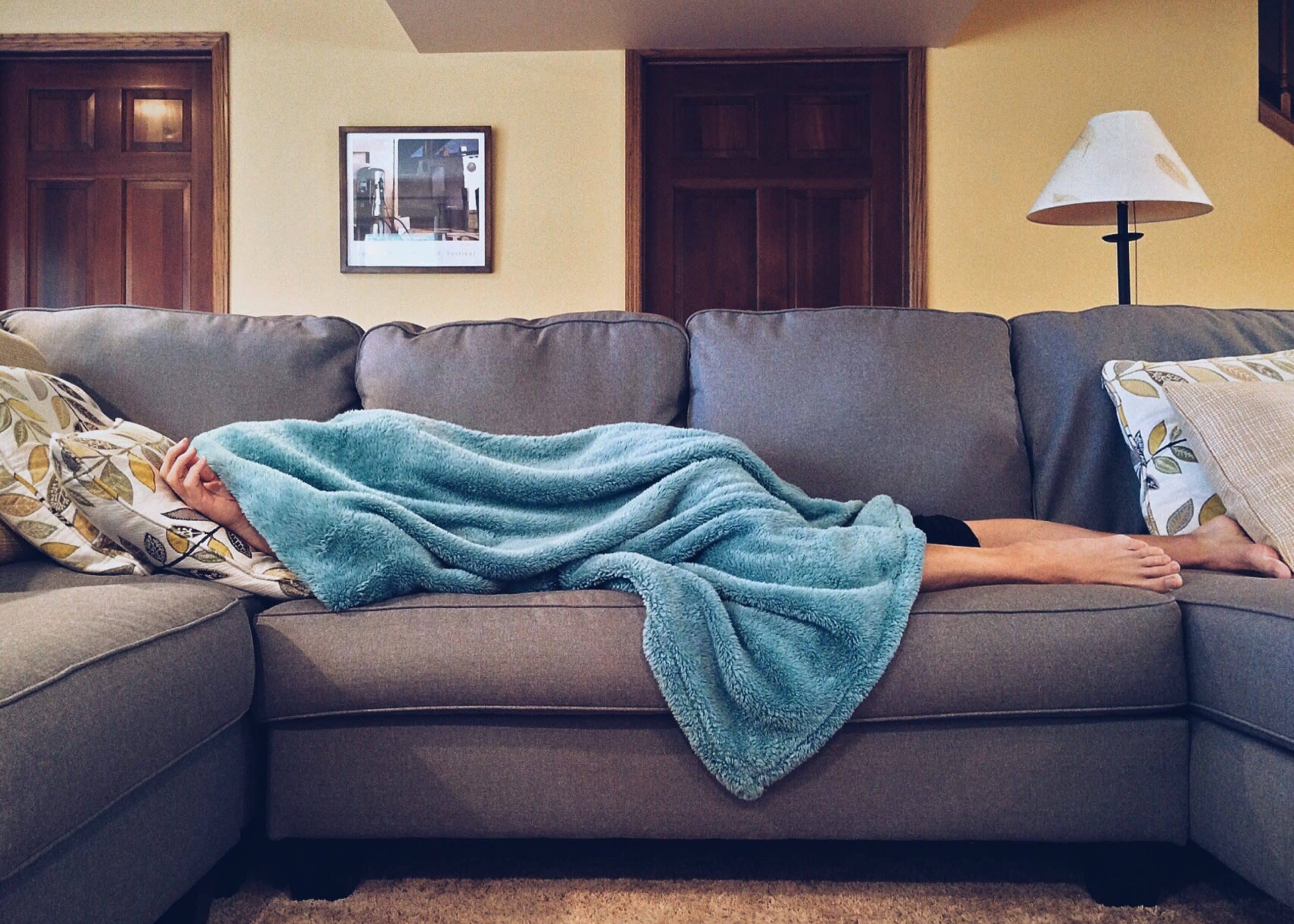 Photo of a person taking a nap on a grey couch with a blue blanket