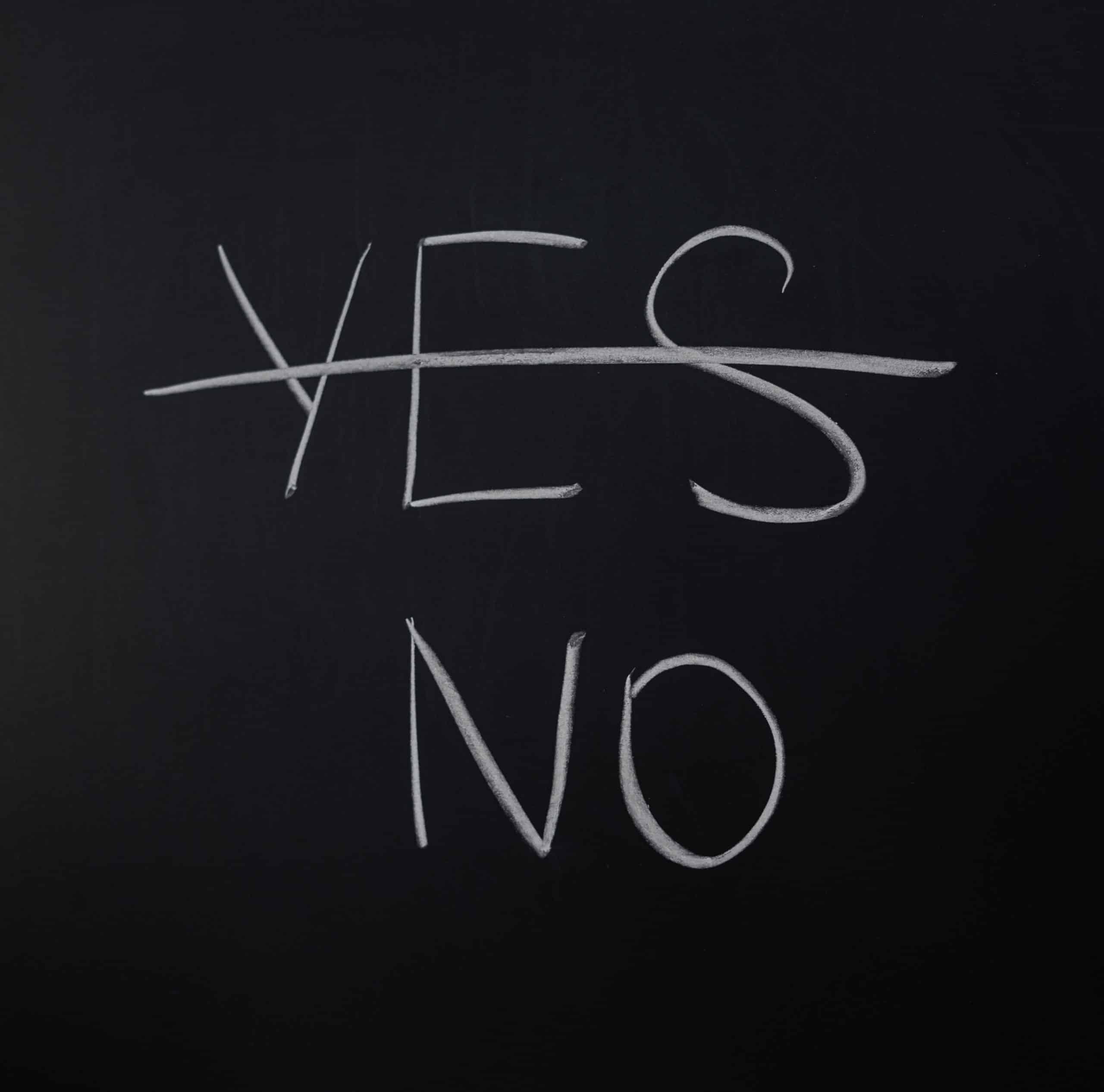 A blackboard. Written in white chalk is the word "Yes", with a line through it. Underneath it is the word "No"