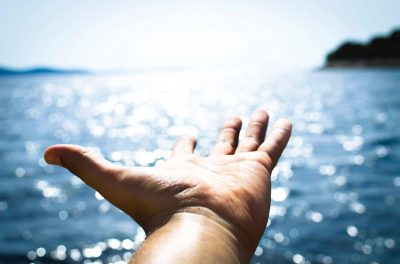 A picture of a hand, palm upward, outstretched towards the horizon, with an ocean in the background..