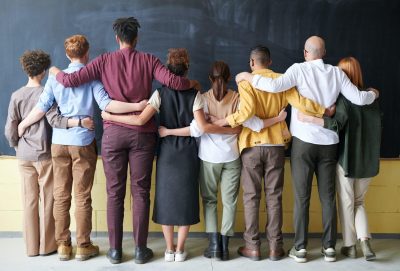 Diverse group of men and women with their arms around each other facing a blackboard