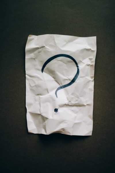 A crumpled piece of paper on a dark background. There is a large question mark on the paper.